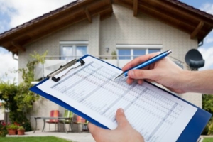 A hand holding a clipboard in front of a two-story home