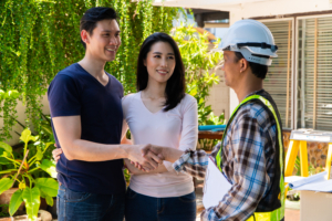 Two homeowners stand in front of a contractor, shaking hands.